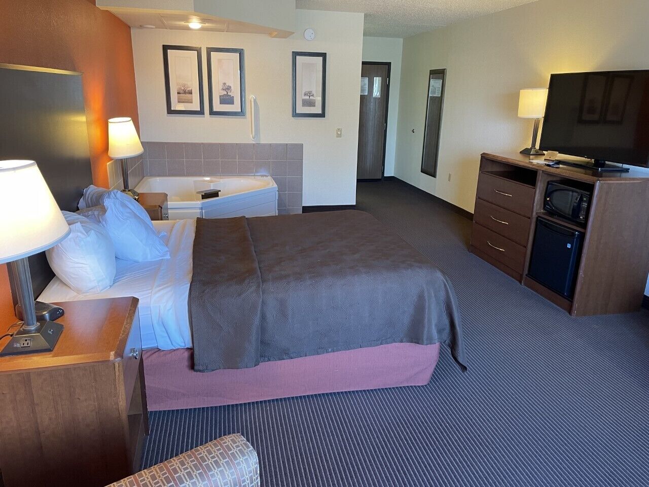 A hotel room with a bed, bedside table, lamp, TV, and a small kitchenette.