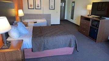 A hotel room with a bed, bedside table, lamp, TV, and a small kitchenette.