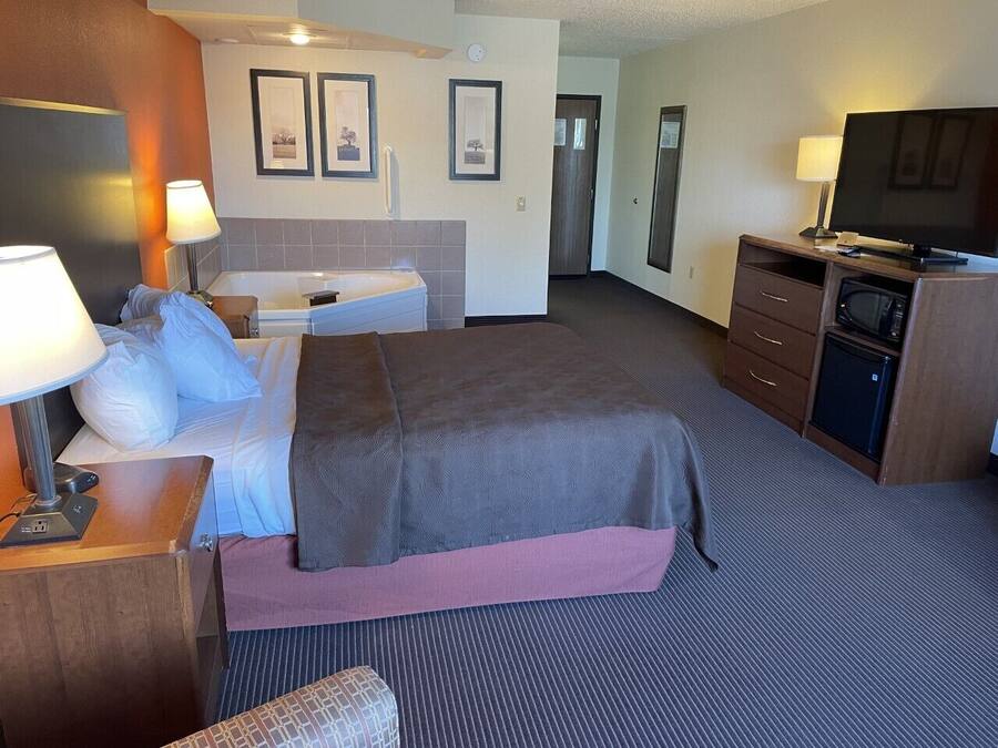 Een hotelkamer met een bed, nachtkastje, lamp, televisie en een kleine kitchenette.