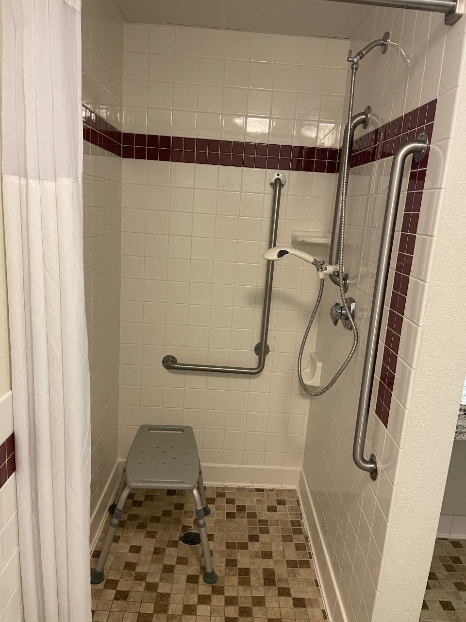 A shower area with a grab bar, a step stool, and a showerhead.