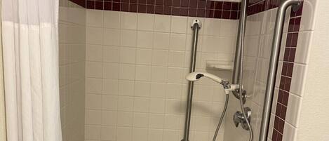 A shower area with a grab bar, a step stool, and a showerhead.