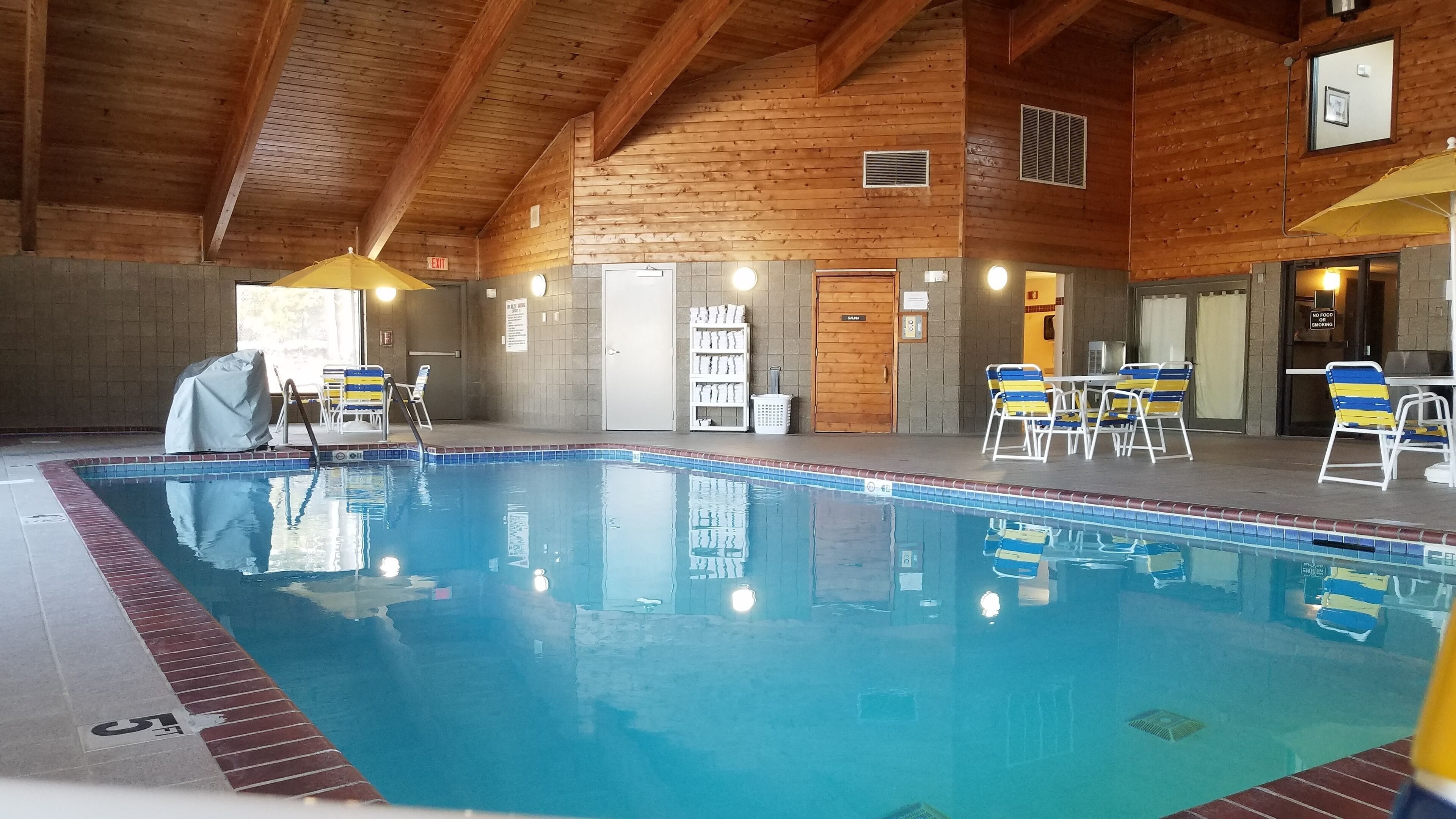 Una piscina interior con paredes de azulejos y vigas de madera, rodeada de sillones de descanso y una zona cubierta.