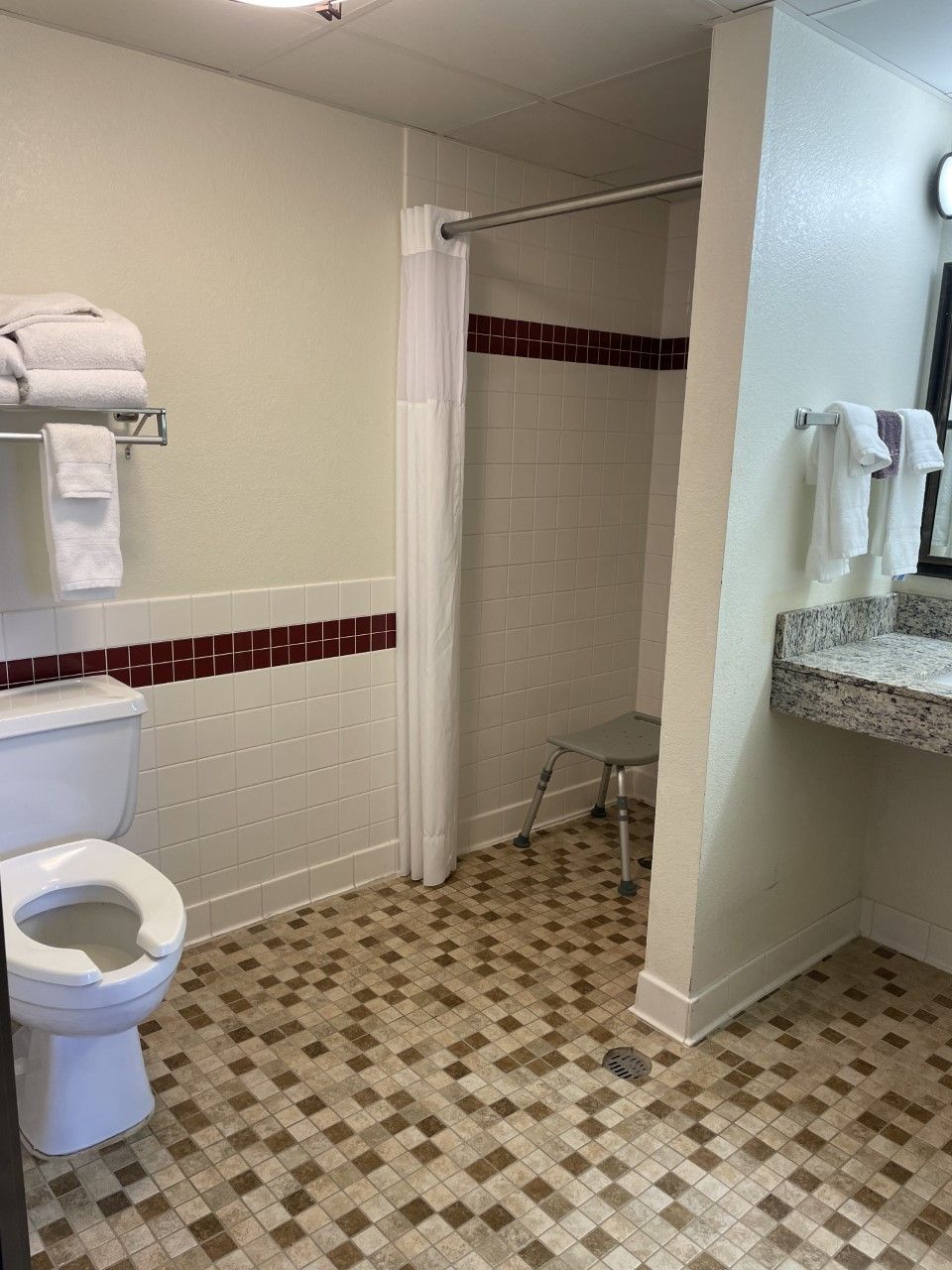 Et badeværelse med toilet, brusekabine med gardin, håndvask med spejl og håndklæder på en hylde.