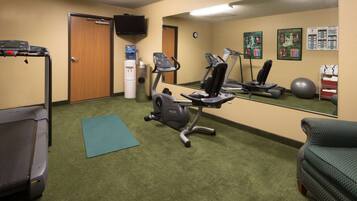 Een sportschool met trainingsapparatuur, een loopband, een crosstrainer, een hometrainer en een yogamat.