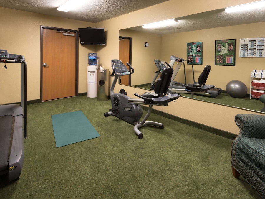 Een sportschool met trainingsapparatuur, een loopband, een crosstrainer, een hometrainer en een yogamat.