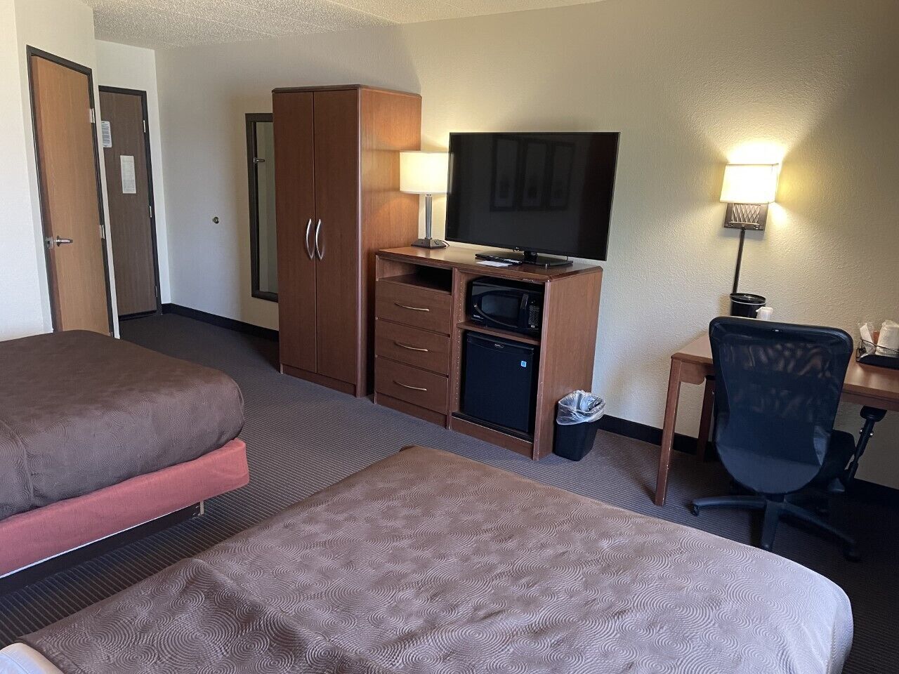 Ein Hotelzimmer mit zwei Betten, einem Schreibtisch mit Computer, einem Fernseher und einem kleinen Kühlschrank.