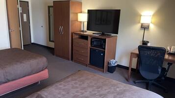 A hotel room with two beds, a desk with a computer, a television, and a small refrigerator.