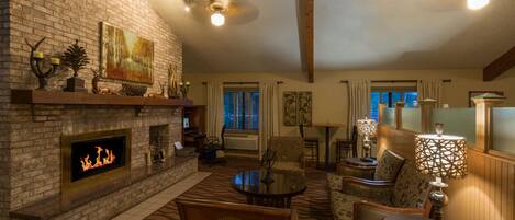A cozy living room with a brick fireplace, comfortable seating, and a large window.