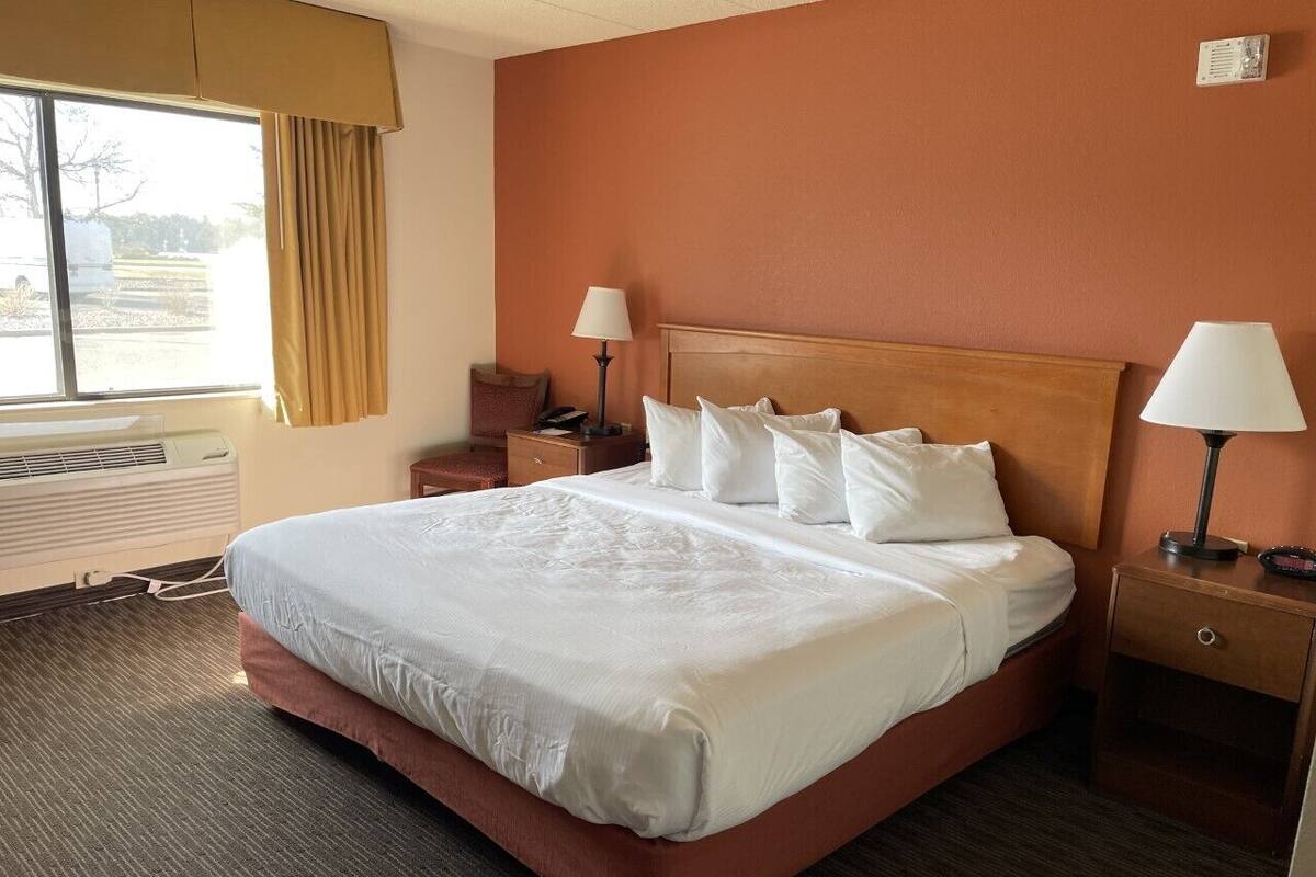 Habitación de hotel con una cama grande, dos mesitas de noche, una ventana con cortinas e un aire acondicionado de pared.