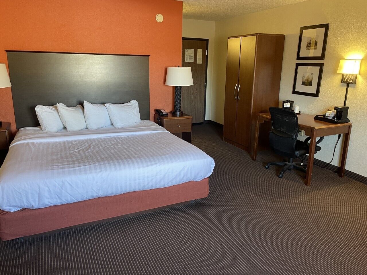 Une chambre d’hôtel avec un grand lit, un bureau, une armoire et une table de chevet avec une lampe.