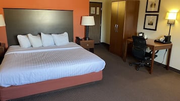 Habitación de hotel con una cama grande, un escritorio, un armario y una mesita de noche con lámpara.