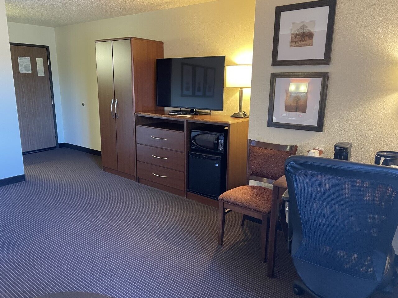 A hotel room with a kitchenette, a television, a desk, and a chair.