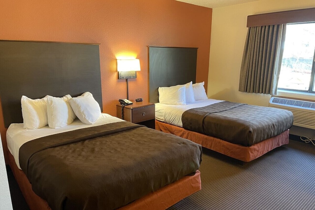 Una habitación de hotel con dos camas, una mesita de noche con lámpara y una ventana con cortinas.