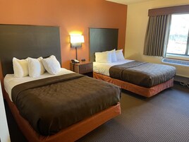 Una habitación de hotel con dos camas, una mesita de noche con lámpara y una ventana con cortinas.