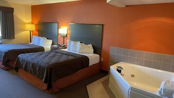 A hotel room with two beds, a large flat-screen TV, a bathtub, and a desk with a lamp.