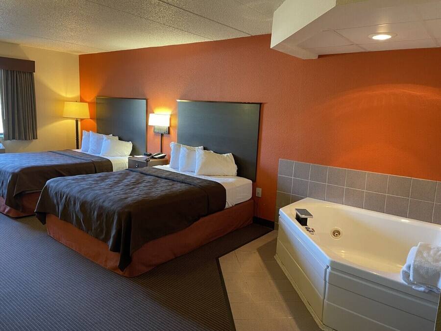A hotel room with two beds, a large flat-screen TV, a bathtub, and a desk with a lamp.