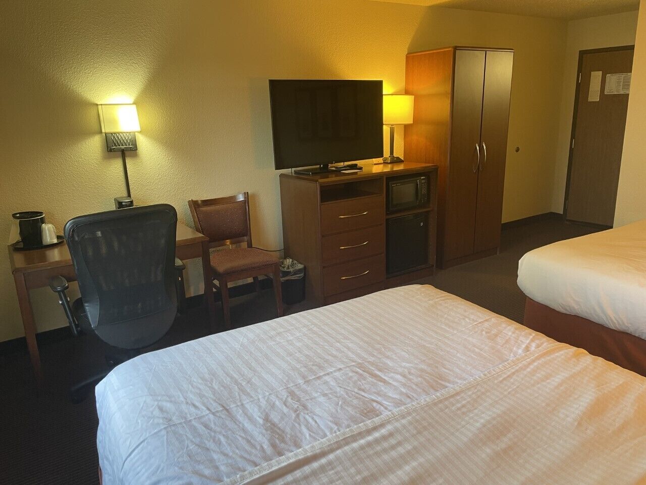 Une chambre d’hôtel avec deux lits, un bureau avec une chaise, une télévision, un four à micro-ondes et une armoire.