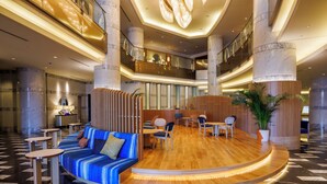 Un vestíbulo amplio con una zona de estar central, una escalera y un entresuelo con barandilla.