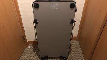 Una silla compacta gris, plegable, con asa y ruedas, ubicada en un pasillo estrecho con puertas de madera y suelo alfombrado.