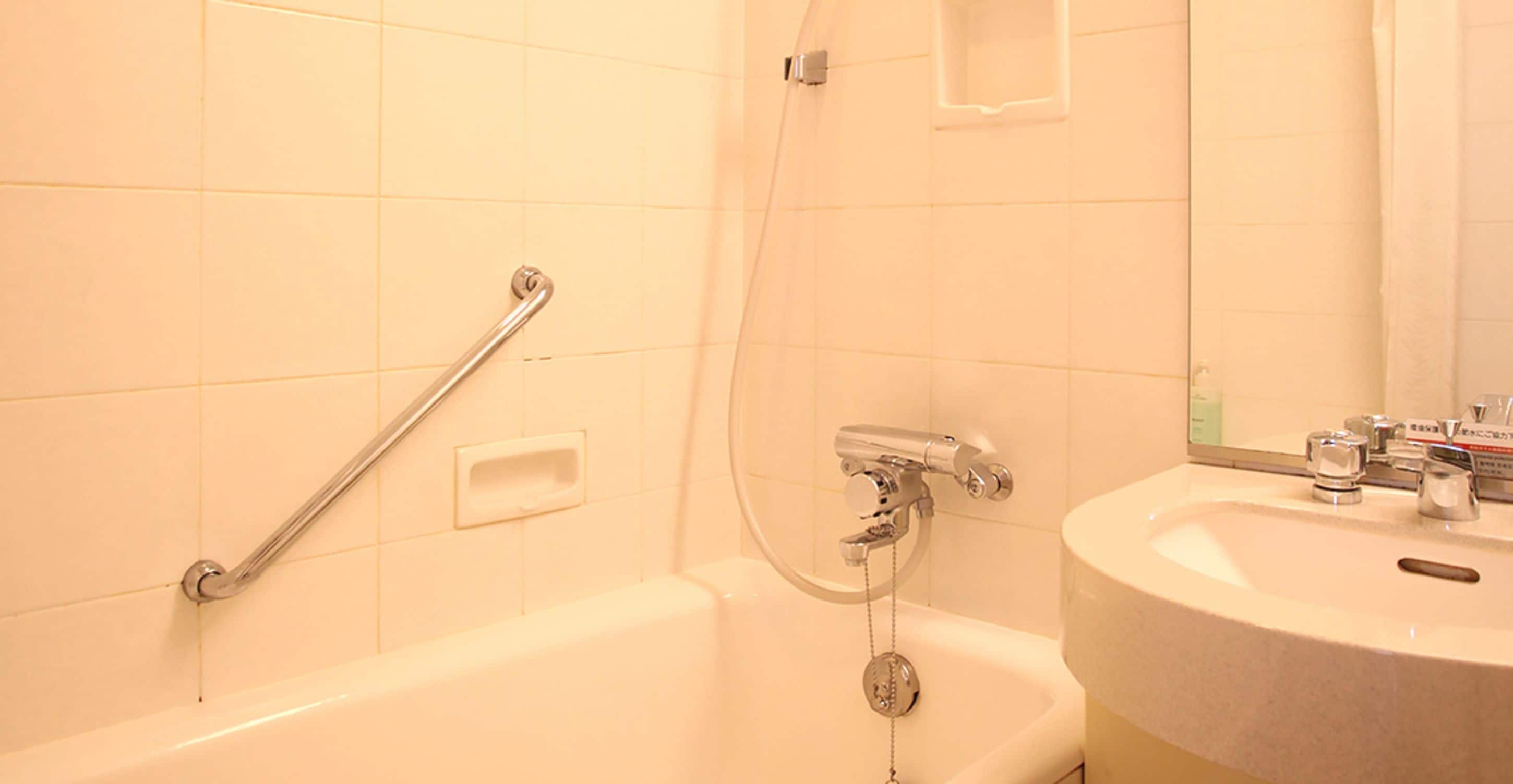 A bathroom with a bathtub, a handrail, a showerhead, a sink, and a mirror.