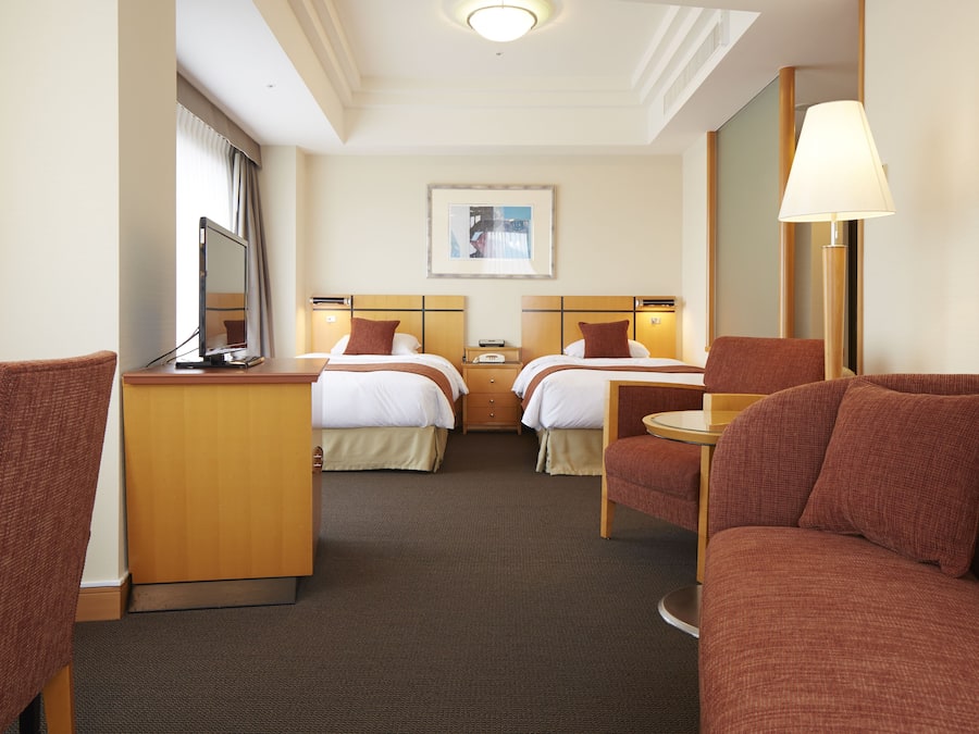 A hotel room with two beds, a desk, a chair, and a sofa.