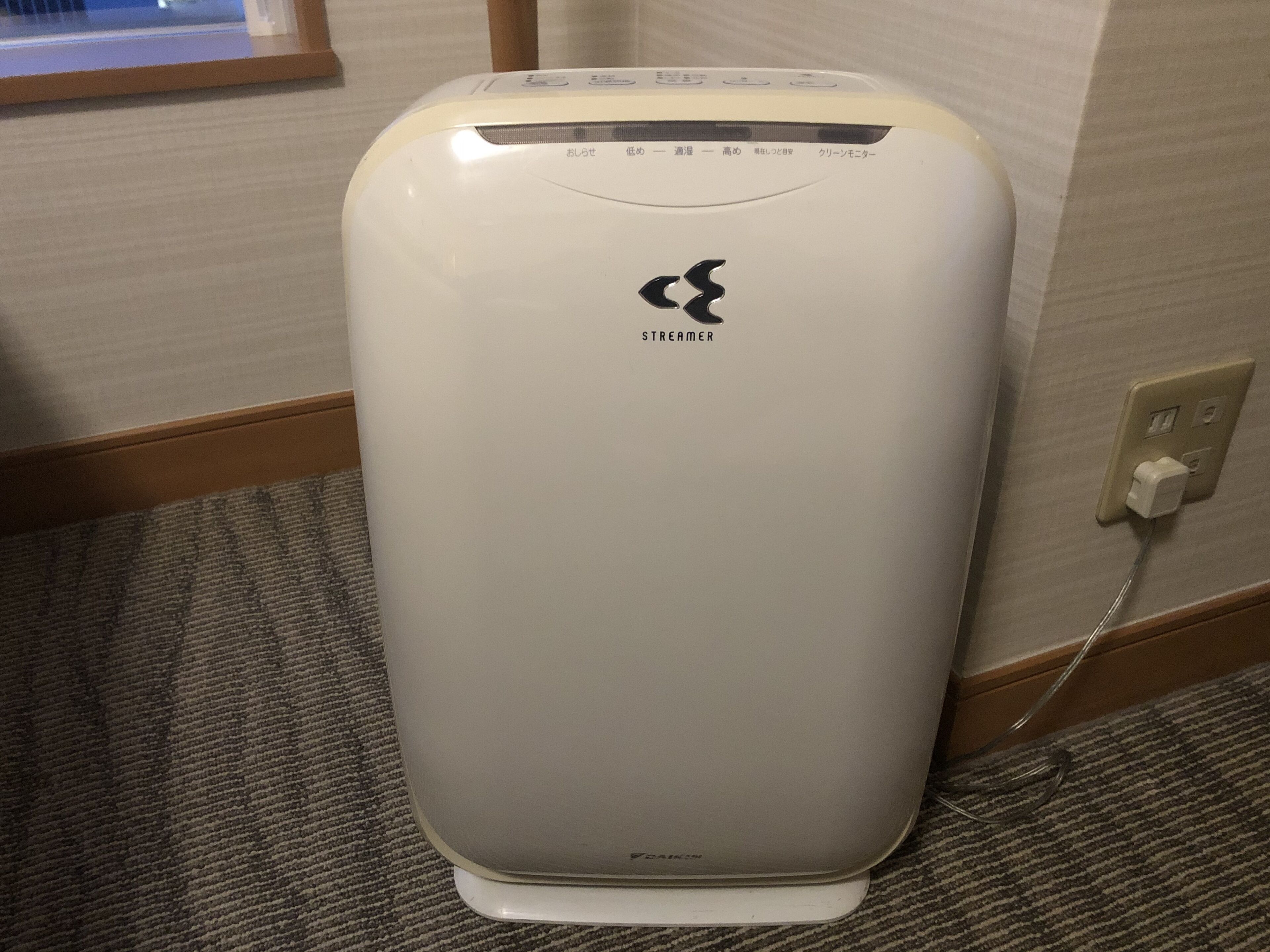 A white portable air conditioner with a control panel and a power cord plugged into a wall socket.