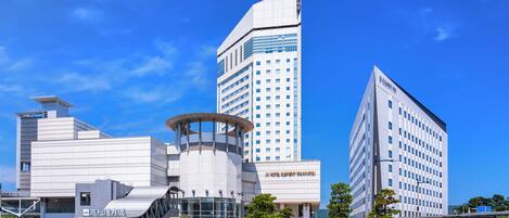 Un hotel moderno con una estructura curva distintiva, una torre destacada y un cielo azul despejado.