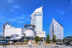 Un hôtel moderne à l’architecture originale, caractérisé par une structure incurvée et une tour imposante, le tout se découpant sur un ciel d’un bleu éclatant.
