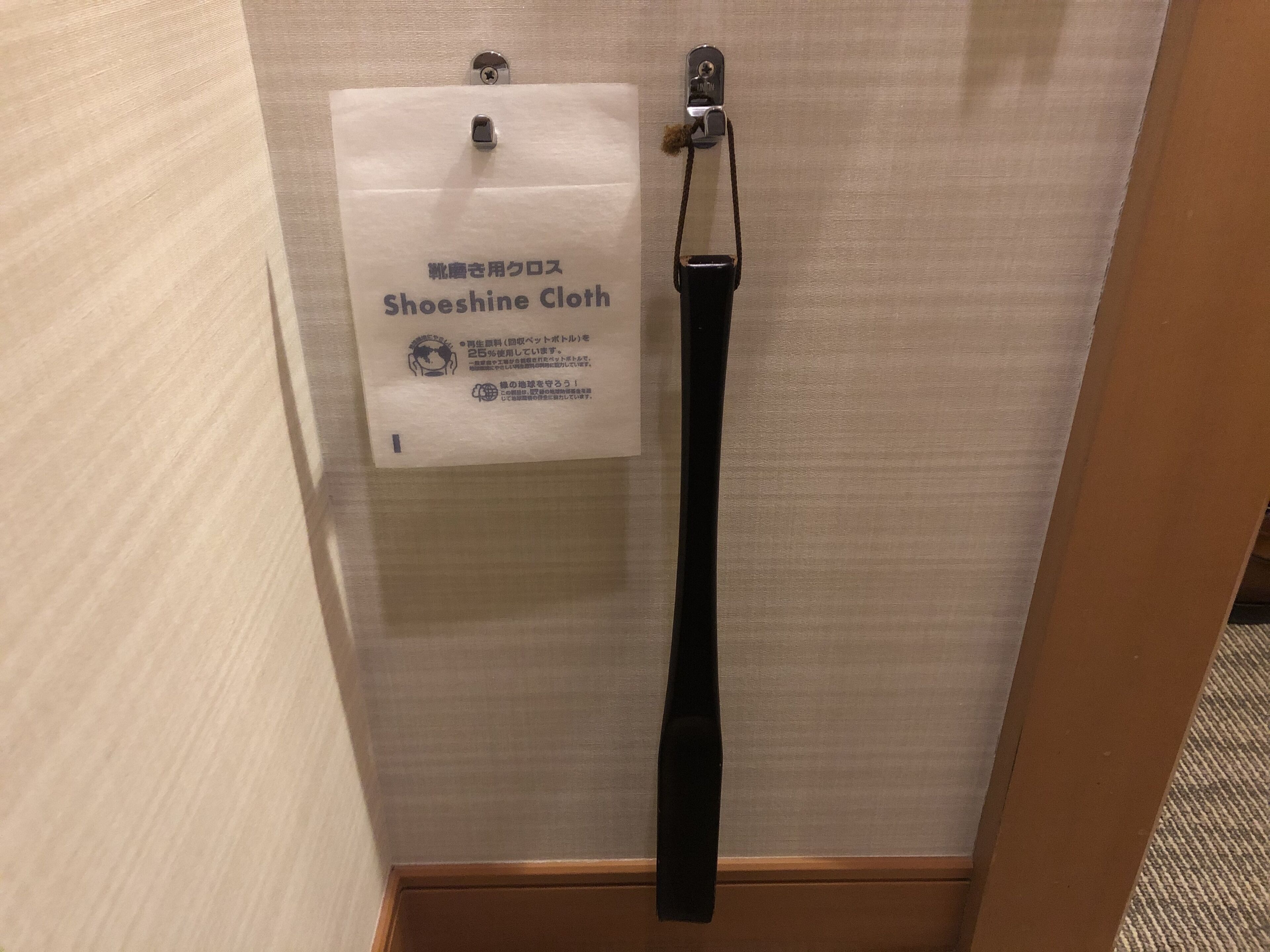 A Shoeshine Cloth hanging on a wall, a metal hook, and a black strap.