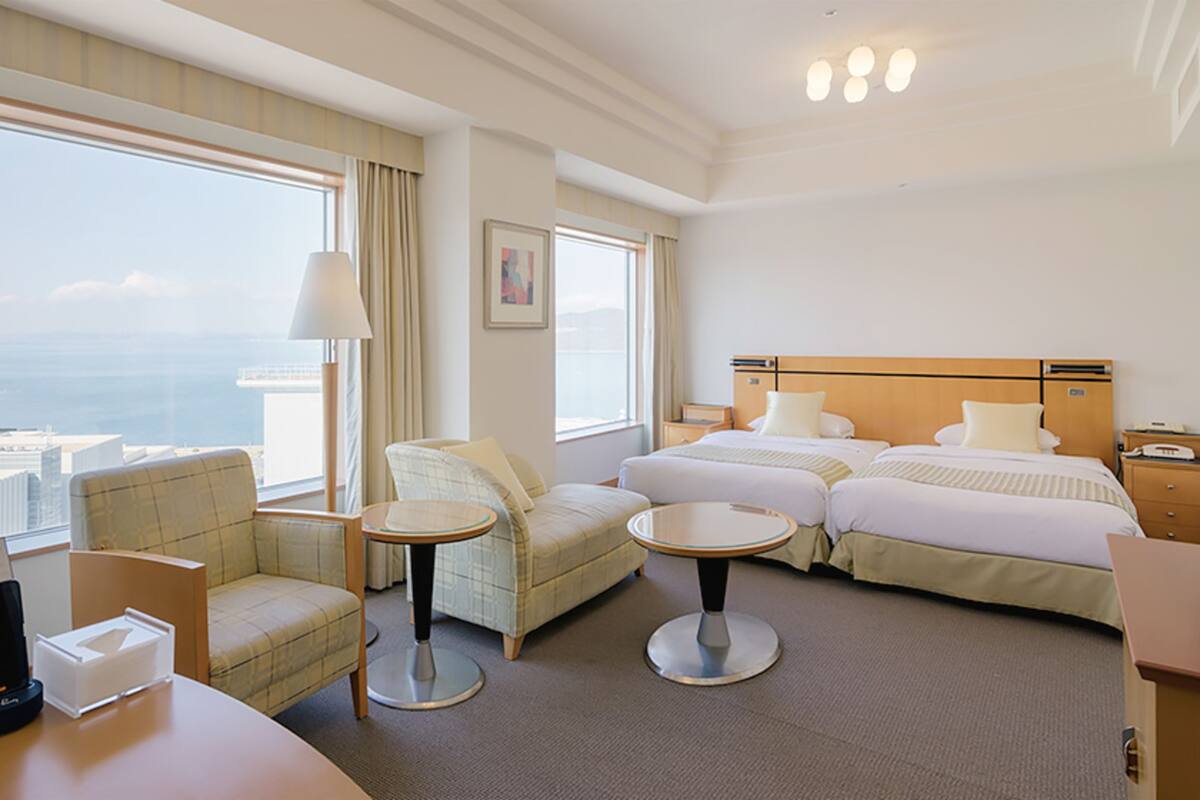 Habitación de hotel con un ventanal grande, una cama, un escritorio, una silla y una mesita.