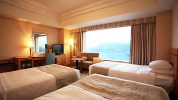 A hotel room with two beds, a desk with a computer, a chair, a small table, and a large window with curtains.