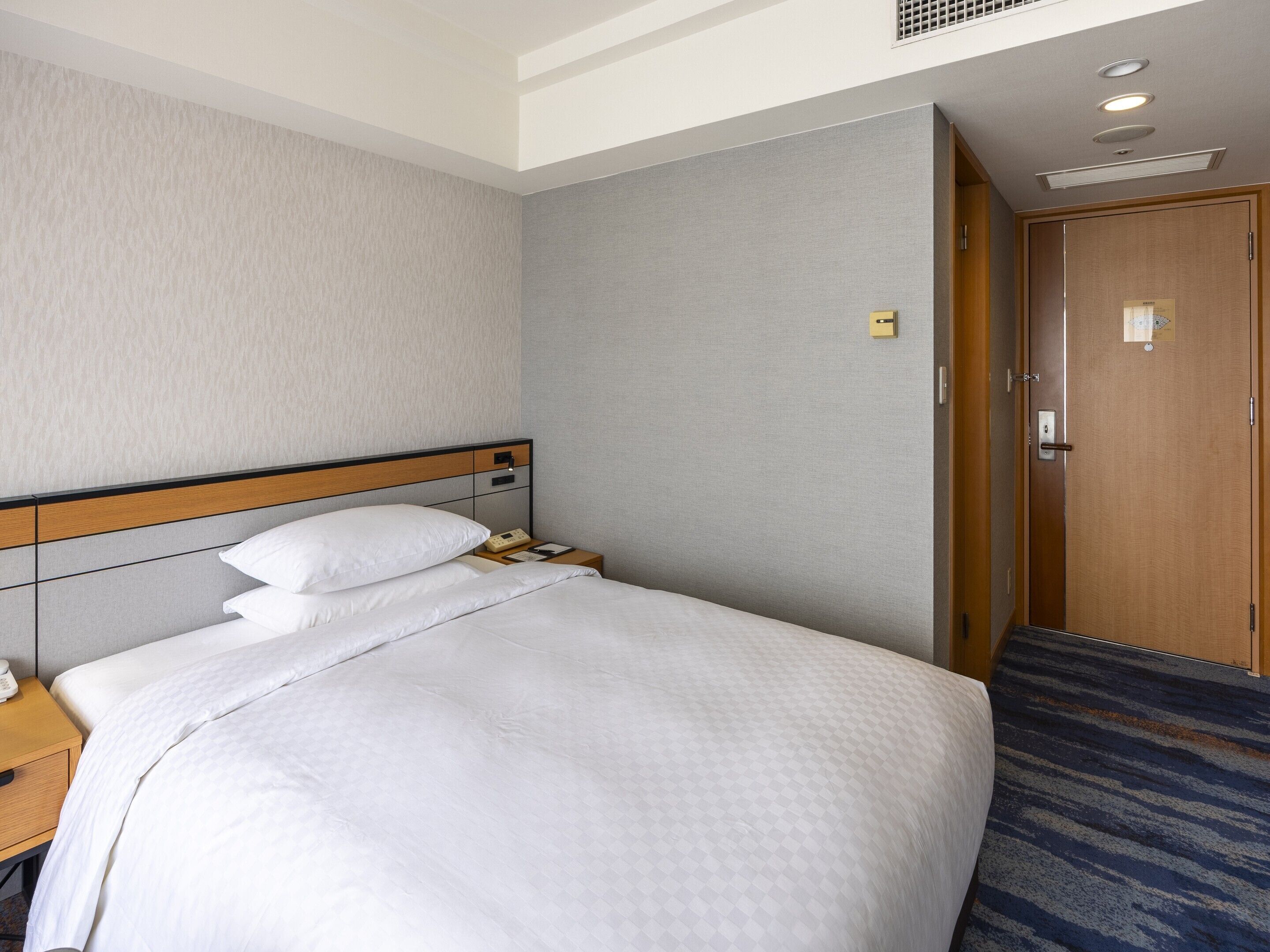A hotel room with a bed, a nightstand, a wooden door, and a carpeted floor.