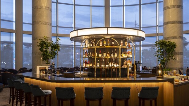 Zona de bar con mostrador central, diversas opciones de asientos y amplios ventanales con vistas a la ciudad.