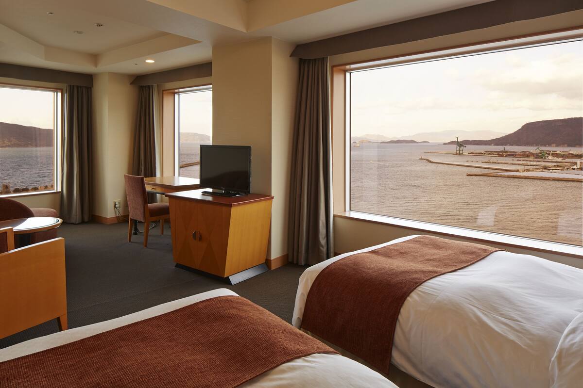 Habitación de hotel con dos camas, un escritorio con televisor y vista al mar.
