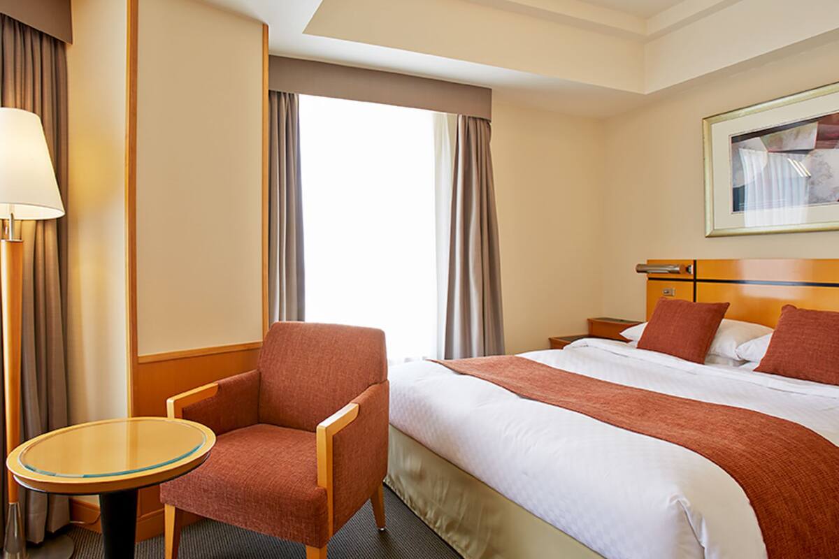 Una habitación de hotel con una cama, una silla, una mesa y una lámpara.
