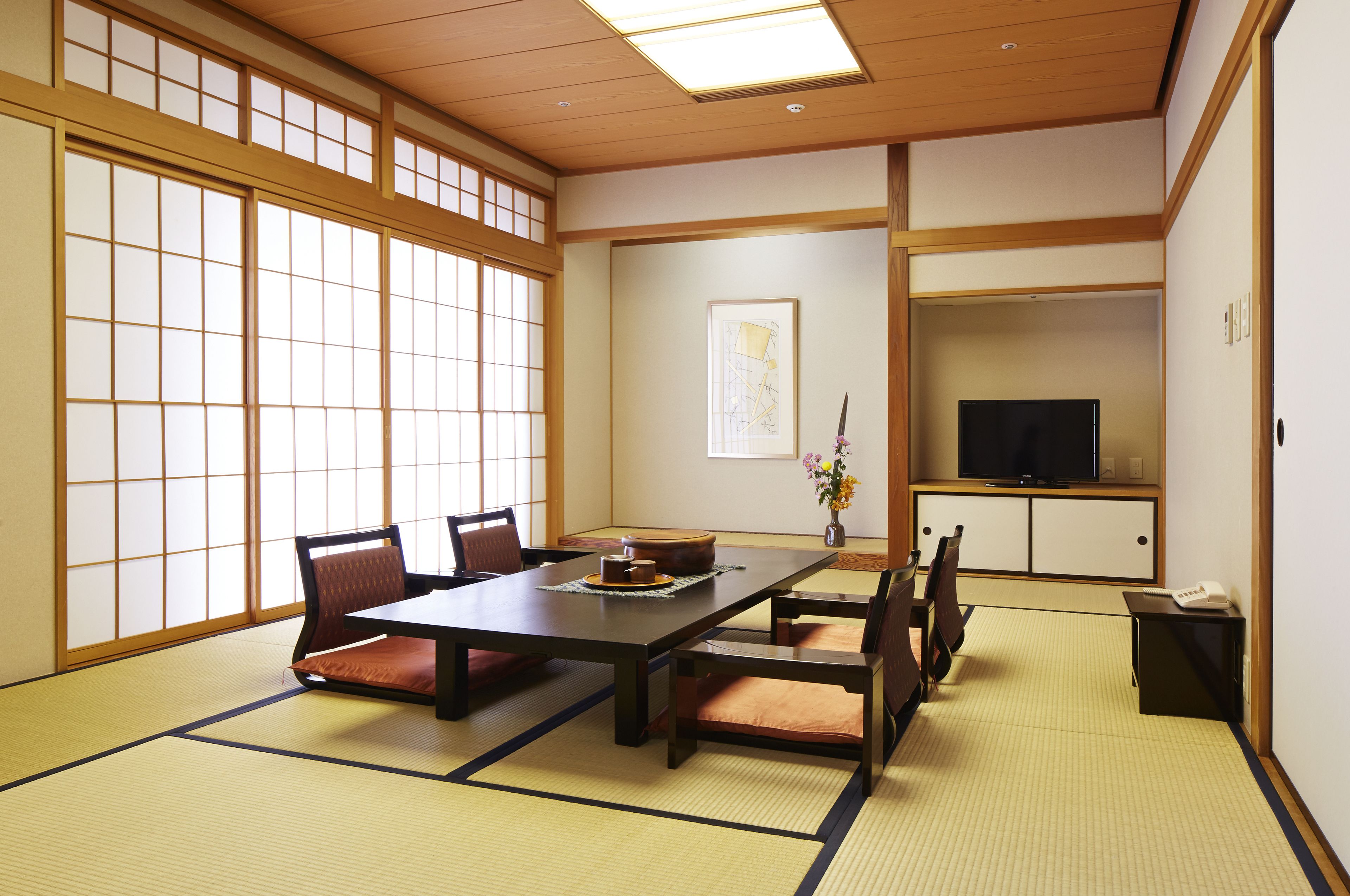 A traditional Japanese room with tatami flooring, a low table with cushions, and a television on a cabinet.