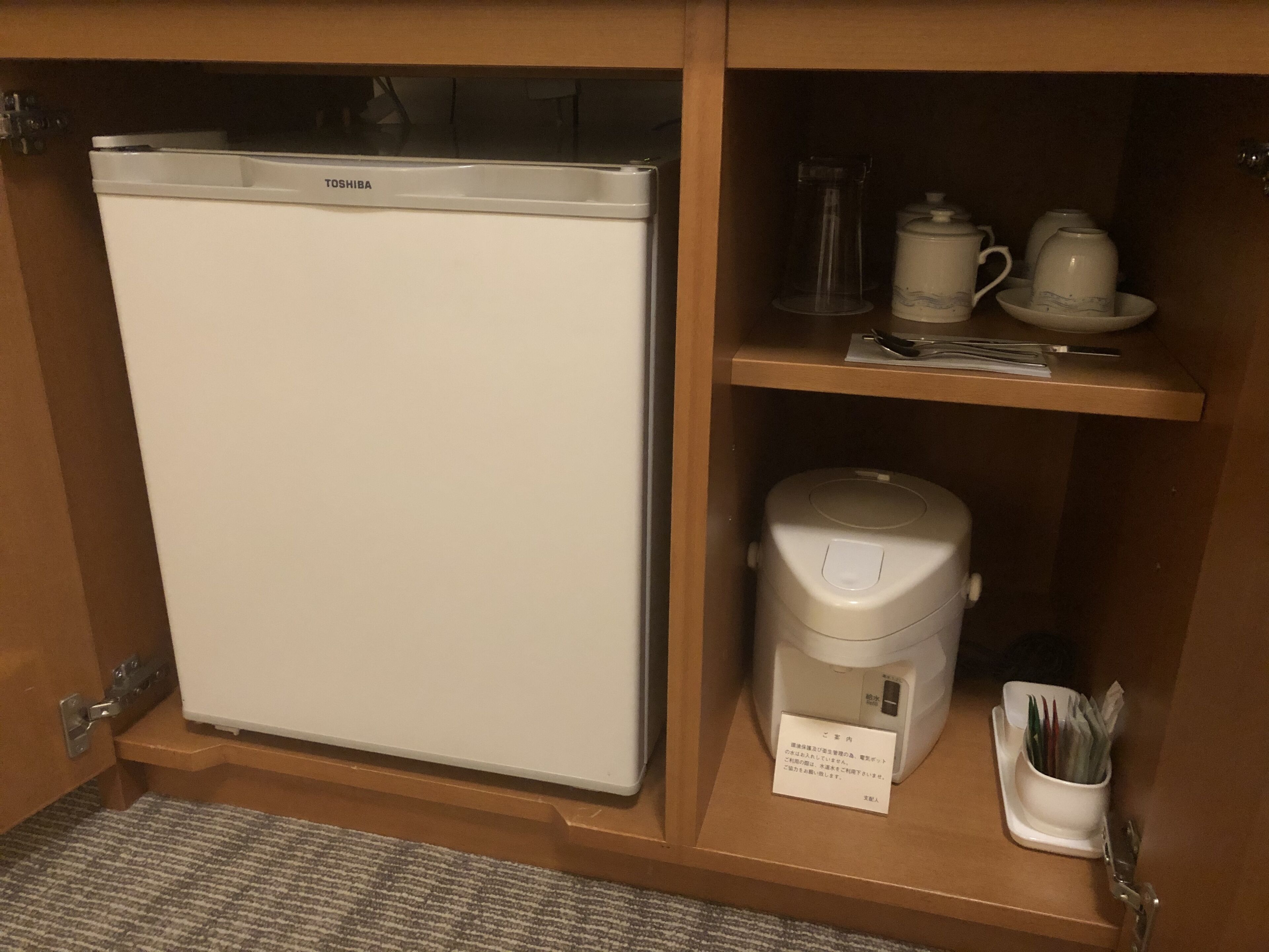 Ein kleiner Kühlschrank mit Toshiba-Logo, eine Kaffeemaschine und ein Teeservice auf einem Regal.