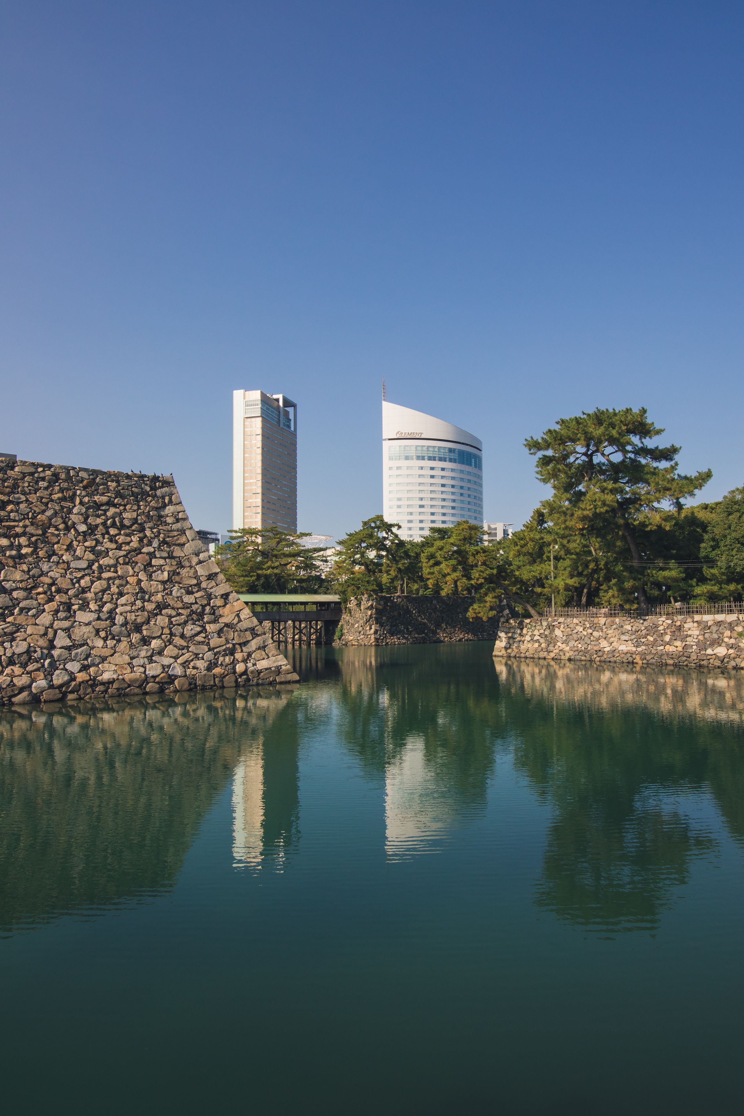 Un lago tranquilo con un muro de piedra y dos edificios modernos al fondo.
