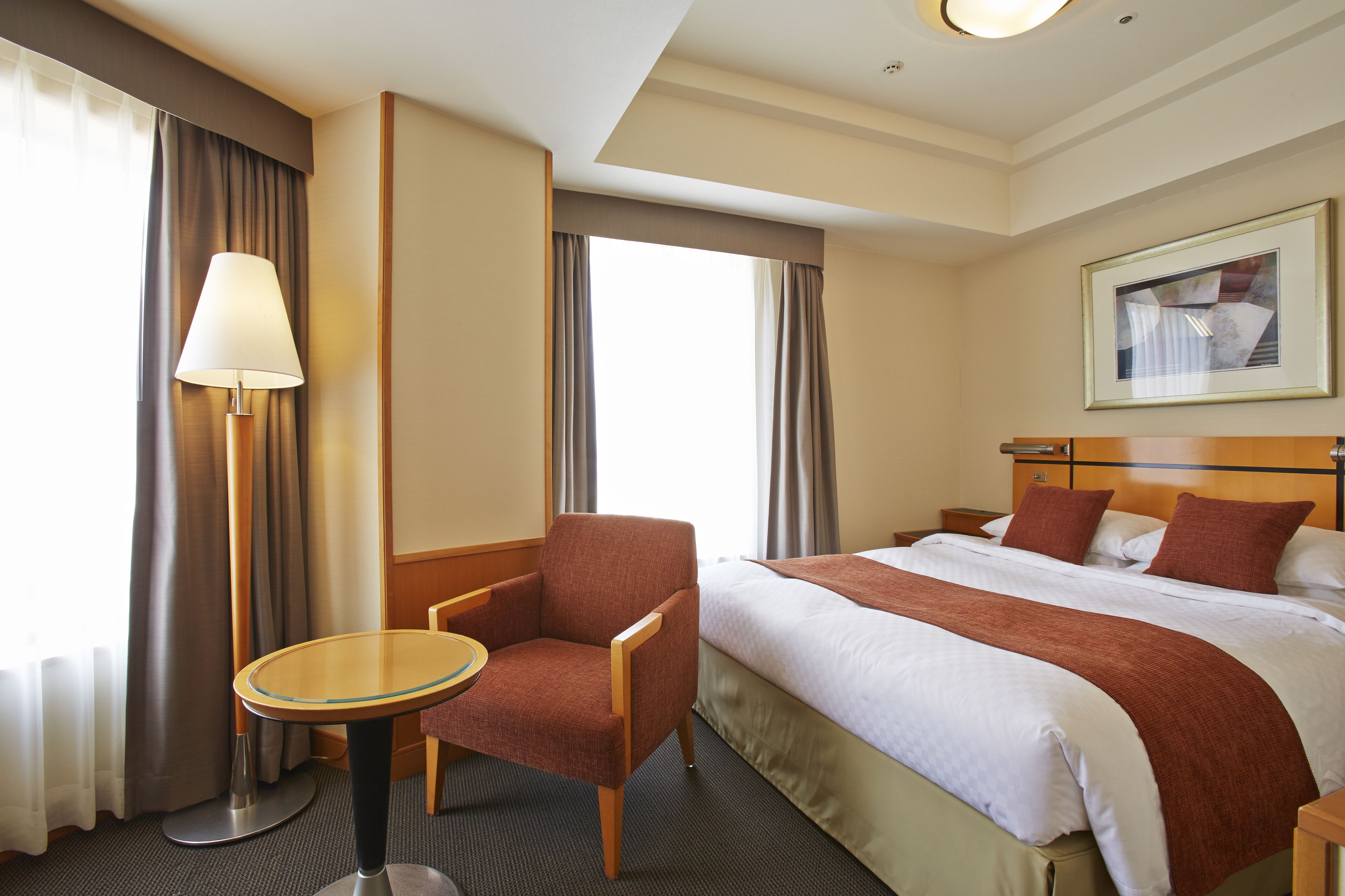 A hotel room with a bed, a chair, a table, and a lamp.