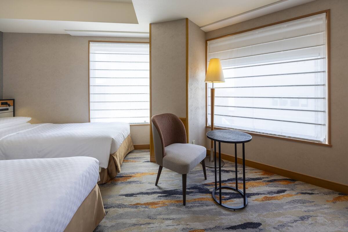 Una habitación de hotel con dos camas, una silla, una mesita y una lámpara.