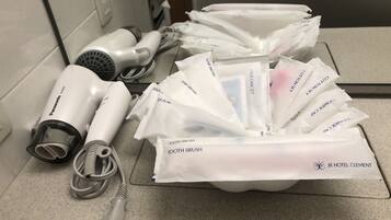A bathroom counter with hair dryers, a hairbrush, and various toiletries like razors, hairbrushes, and a toothbrush.