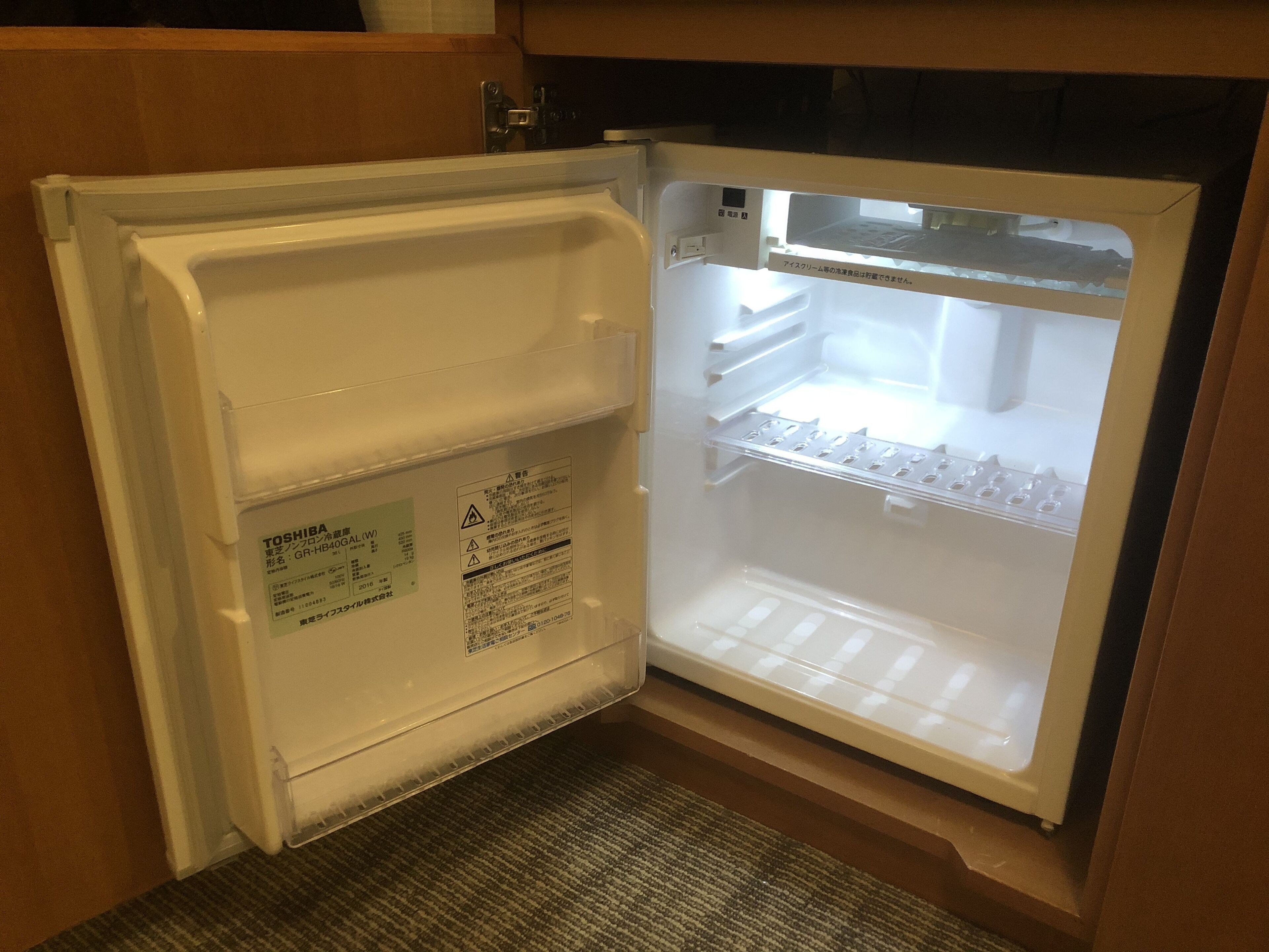 Un refrigerador abierto con una etiqueta que indica que es modelo Toshiba, y una etiqueta de advertencia en la puerta.