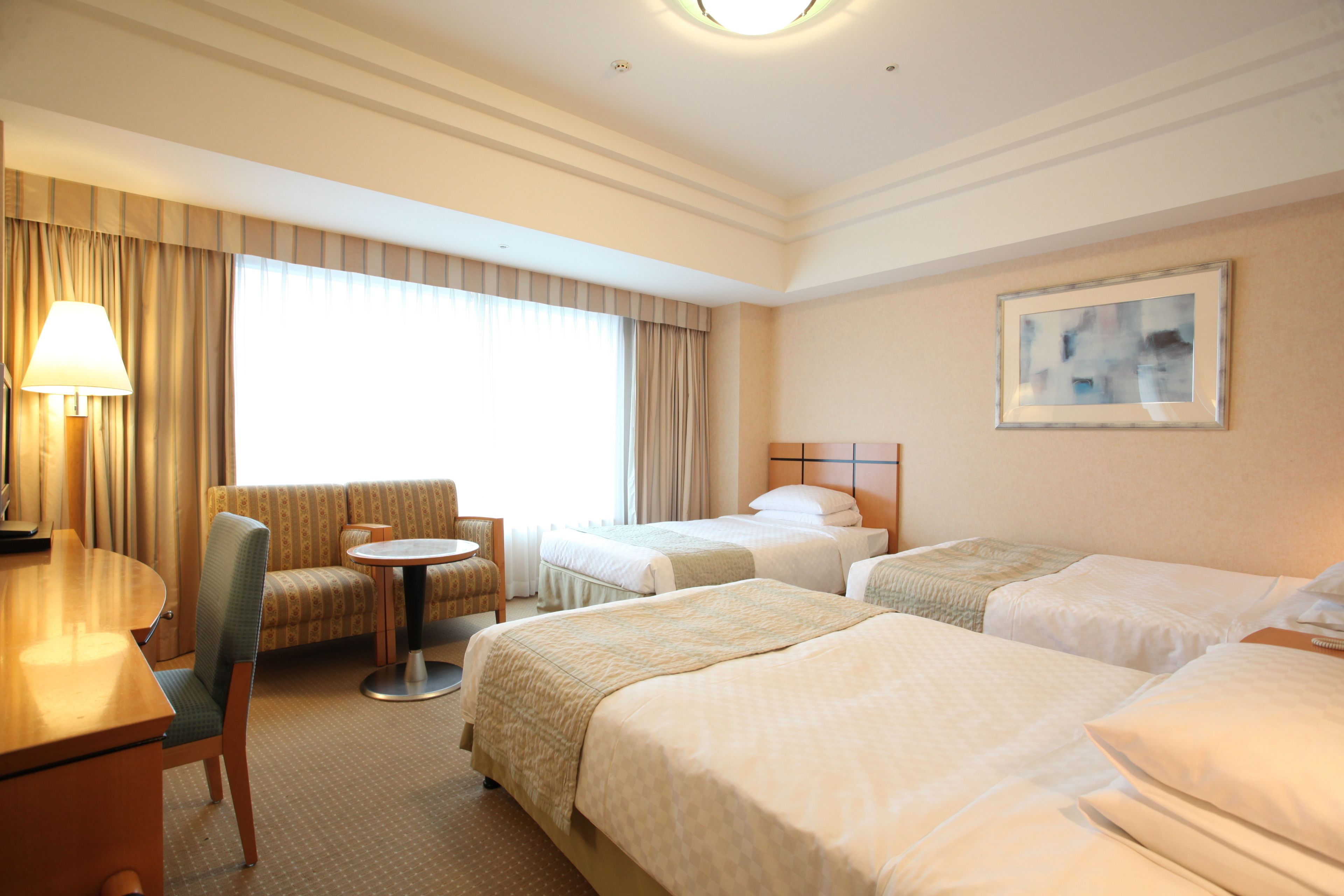 A hotel room with two beds, a sofa, a small round table, and a lamp.