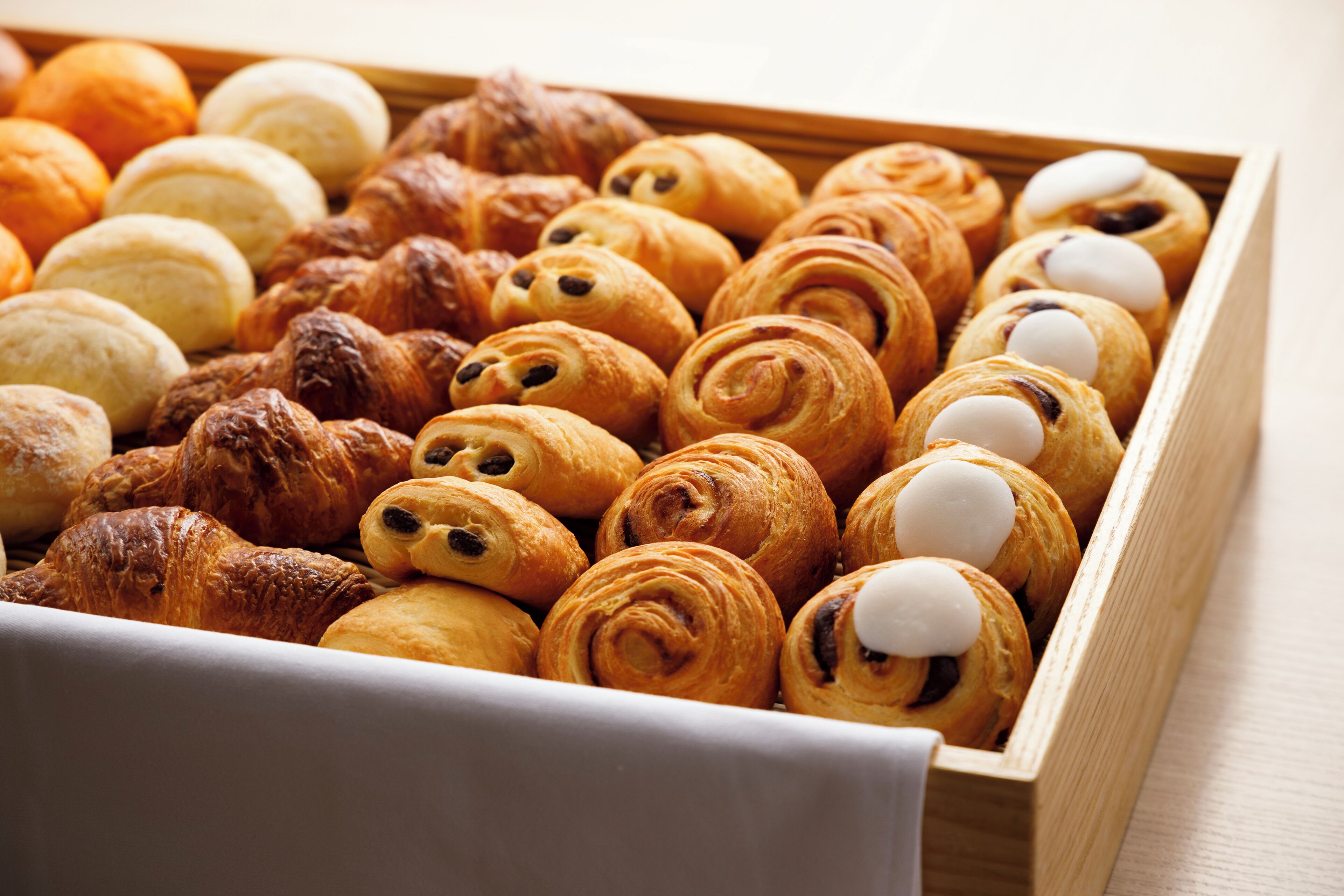 Una caja de madera llena de varios tipos de pasteles, incluyendo cruasanes y muffins.