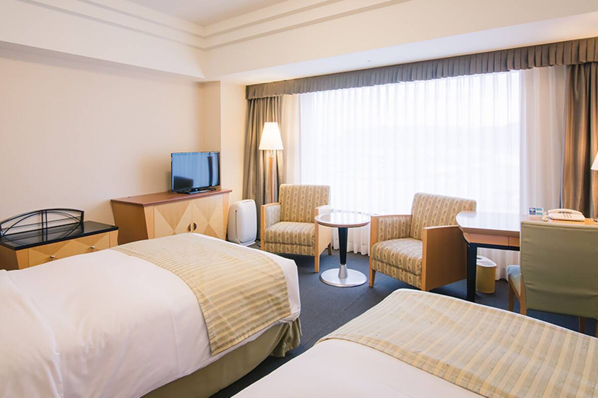 Habitación de hotel con dos camas, un escritorio, una silla, un televisor y una ventana con cortinas.