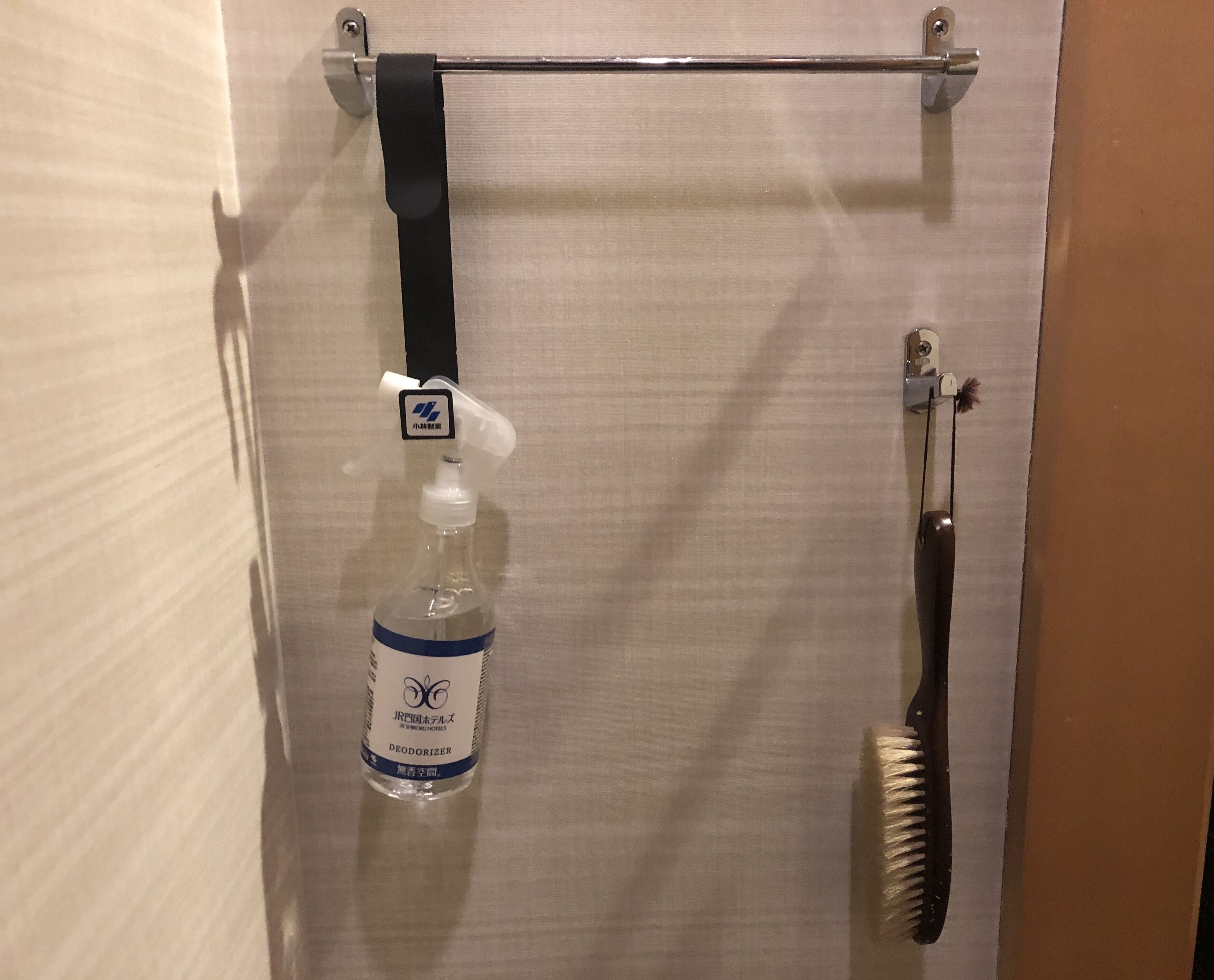 A deodorizer bottle and a brush hanging on a wall.