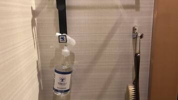 A deodorizer bottle and a brush hanging on a wall.