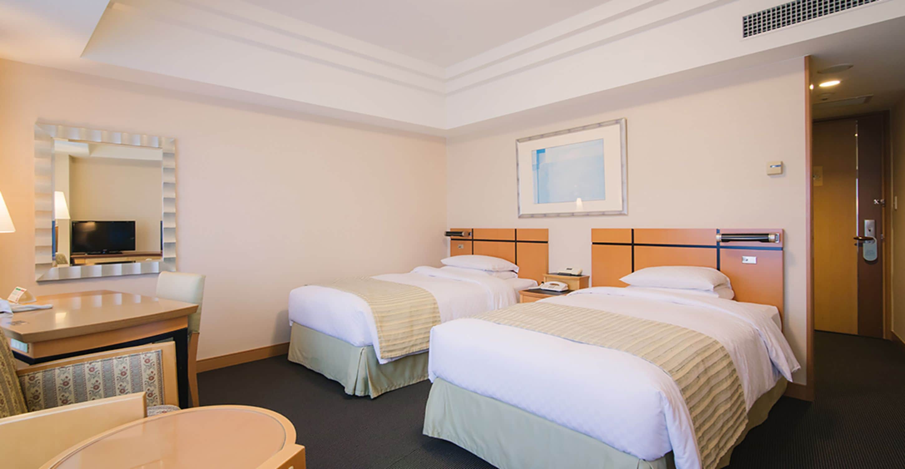 A hotel room with two beds, a desk with a mirror, a TV, and a framed picture on the wall.