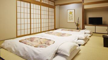 Una habitación japonesa tradicional con suelo de tatami, un futón, un televisor y un jarrón con flores.