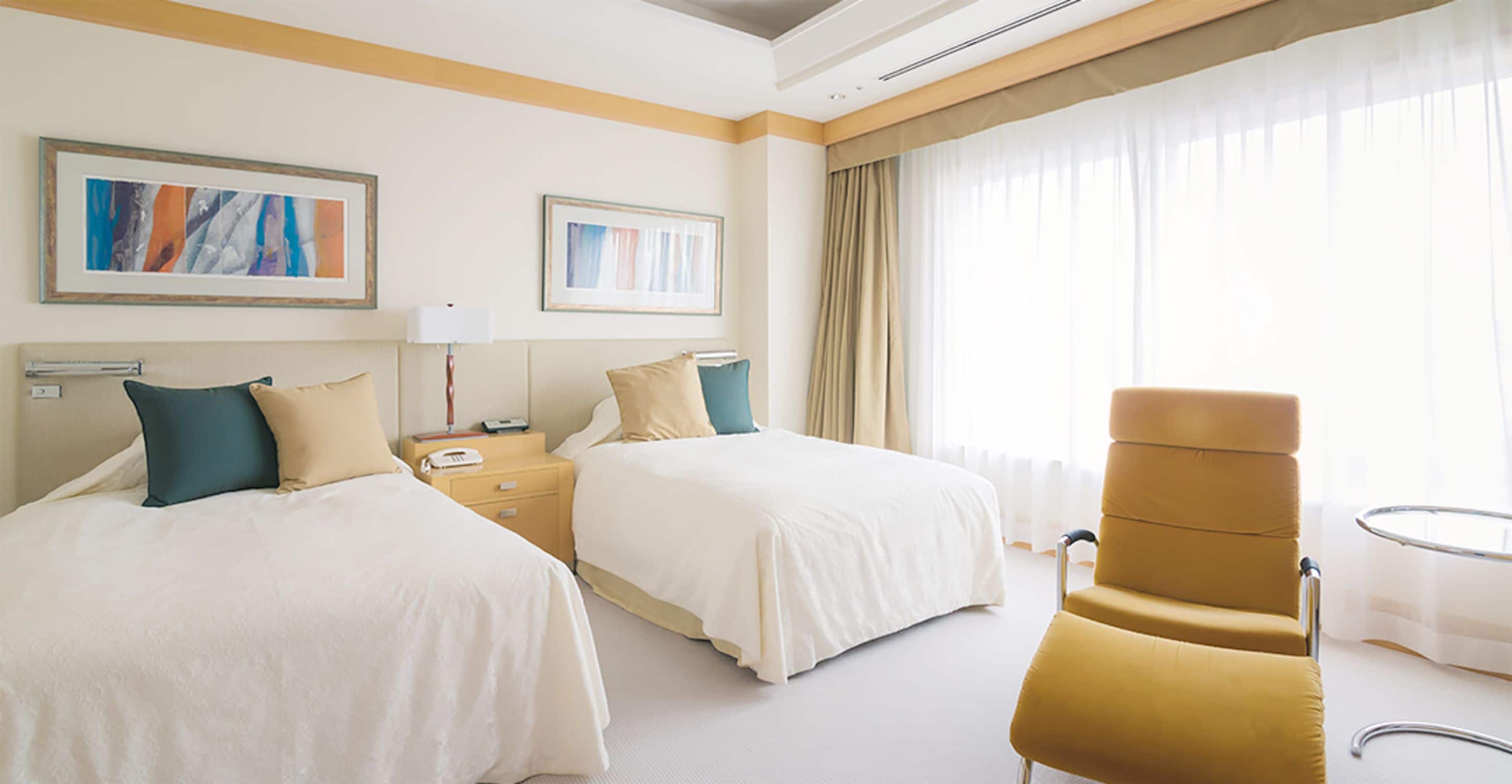 A hotel room with two beds, a chair, a nightstand, and a window with curtains.